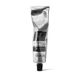 Un tubo plateado arrugado de Resurrection Aromatique Hand Balm de Aesop, apoyado sobre su tapon negro, sobre un fondo blanco.
