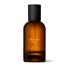 Amber glass Aesop Unforeseen Aer Eau de Parfum bottle with black cap on a white background.