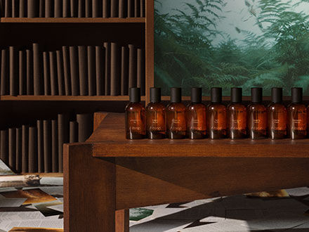 Botellas de vidrio ambar alineadas en una mesa de madera en una habitacion con estanteria y mural de bosque.