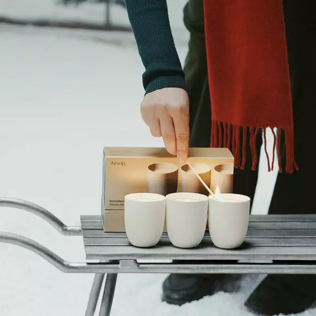 Una mano enciende una vela de un set de regalo de Aesop.
