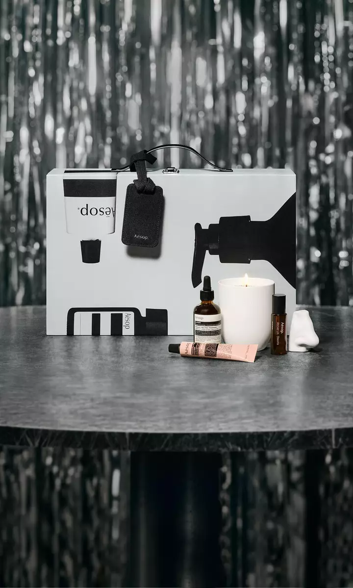 Estuche de regalo y productos de cuidado facial Aesop sobre una mesa, con un fondo festivo de luces suaves.