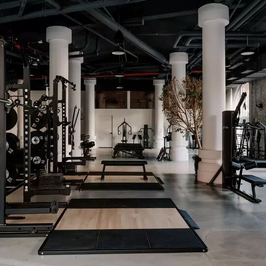 A modern gym with striking finishes: polished concrete floors, white pillars and black equipment.