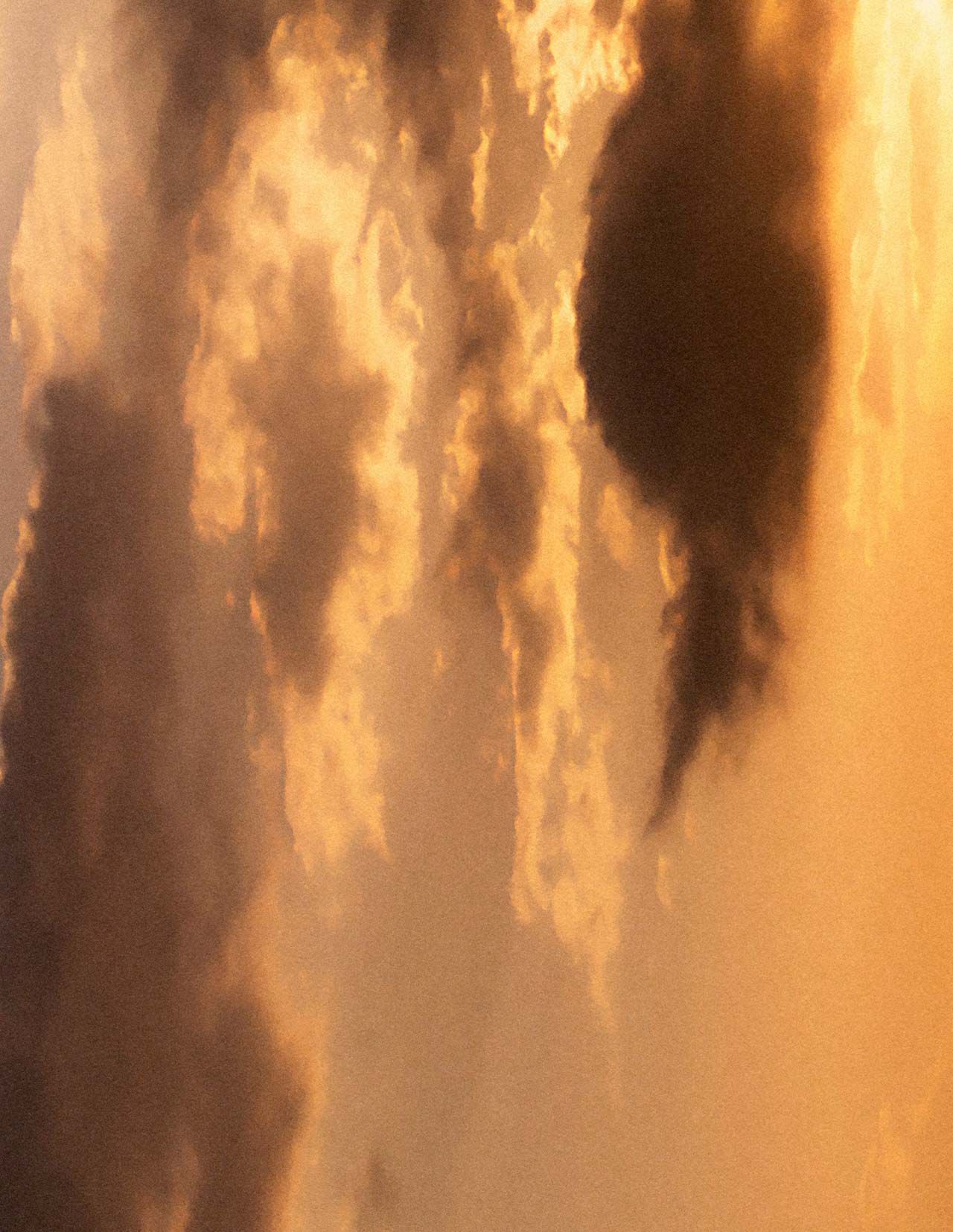 Cielo dorado al atardecer, con nubes estratificadas en calidos tonos ambar, luz suave y difusa, y formas nubosas mas oscuras atravesando la escena.