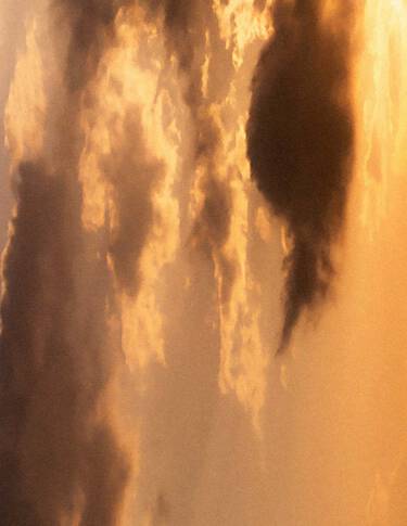 Cielo dorado al atardecer, con nubes estratificadas en calidos tonos ambar, luz suave y difusa, y formas nubosas mas oscuras atravesando la escena.