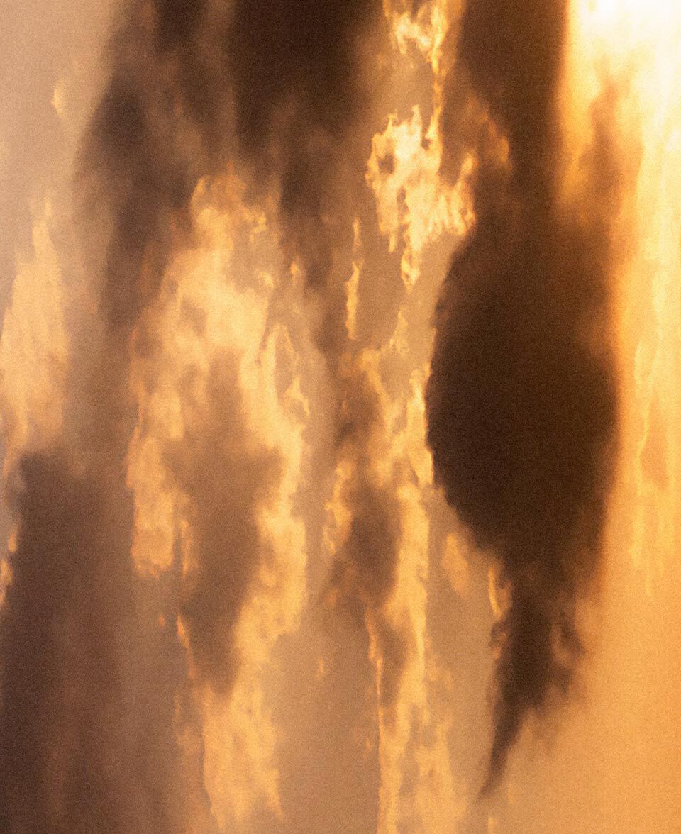Una nube luminosa se forma bajo una calida luz anaranjada, evocando humo y un cielo iluminado por el fuego.