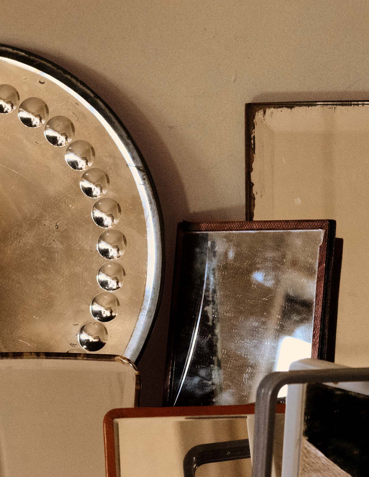 Objetos apilados de metal y piedra en tonos bronce, beige y marron oscuro, dispuestos como formas geometricas superpuestas contra una pared neutra.