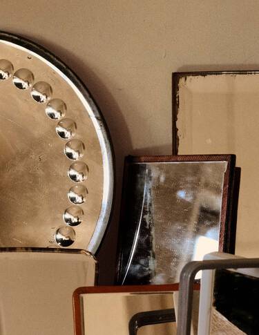 Objetos apilados de metal y piedra en tonos bronce, beige y marron oscuro, dispuestos como formas geometricas superpuestas contra una pared neutra.