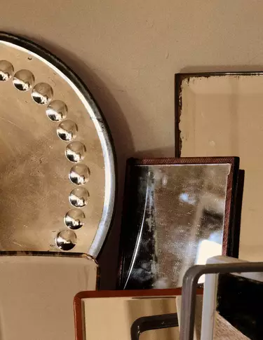 Objetos apilados de metal y piedra en tonos bronce, beige y marron oscuro, dispuestos como formas geometricas superpuestas contra una pared neutra.