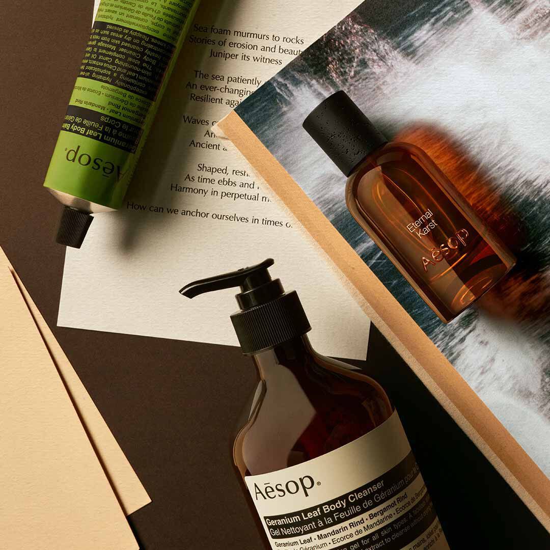 Frasco de Aesop Eternal Karst con dispensador y tubo verde, dispuestos sobre papeles con imagenes de agua espumosa.
