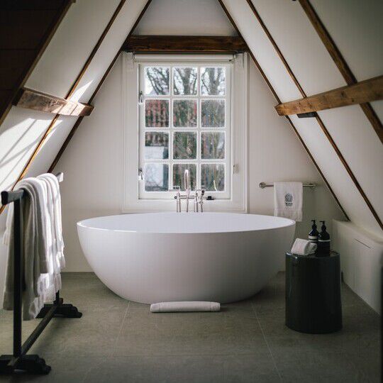 A freestanding bathtub in front of a window, alongside Aesop formulations all under an A-frame ceiling.