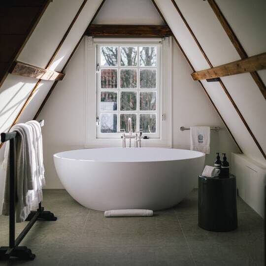 A freestanding bathtub in front of a window, alongside Aesop formulations all under an A-frame ceiling.