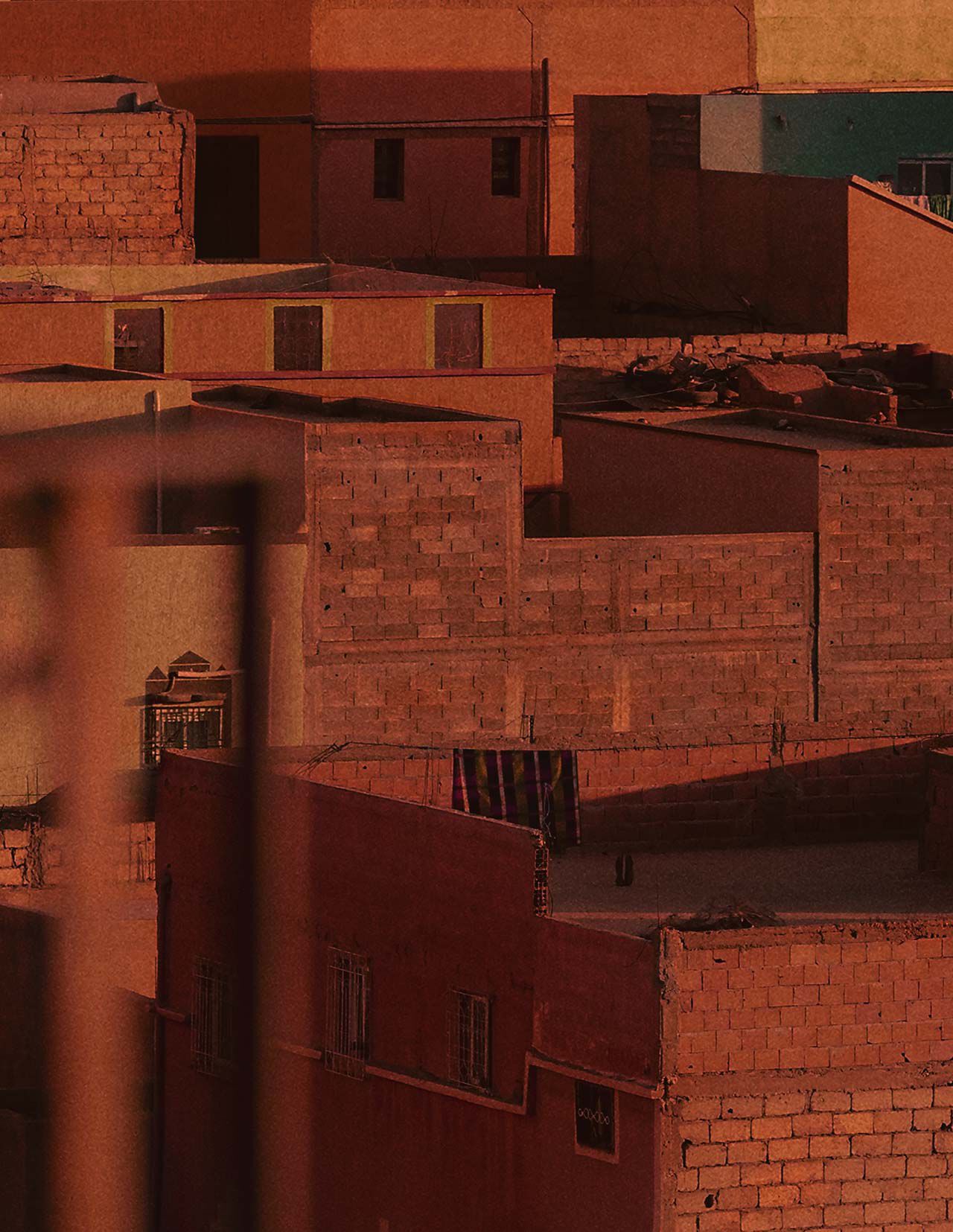 Azoteas y muros de terracota urbanos bajo una calida luz rojo oxido, con arquitectura maciza, fachadas en sombra y superficies de mamposteria texturizada.