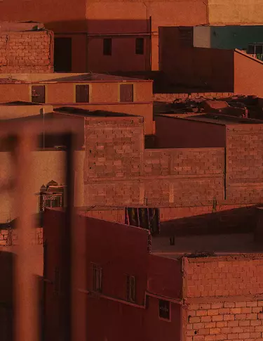 Azoteas y muros de terracota urbanos bajo una calida luz rojo oxido, con arquitectura maciza, fachadas en sombra y superficies de mamposteria texturizada.