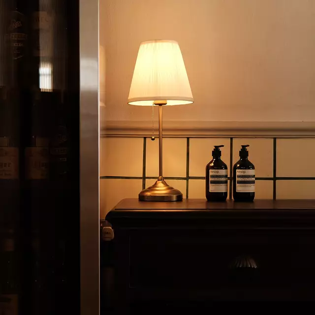 Dos frascos de Aesop sobre una mesa de entrada, junto a una lampara antigua.
