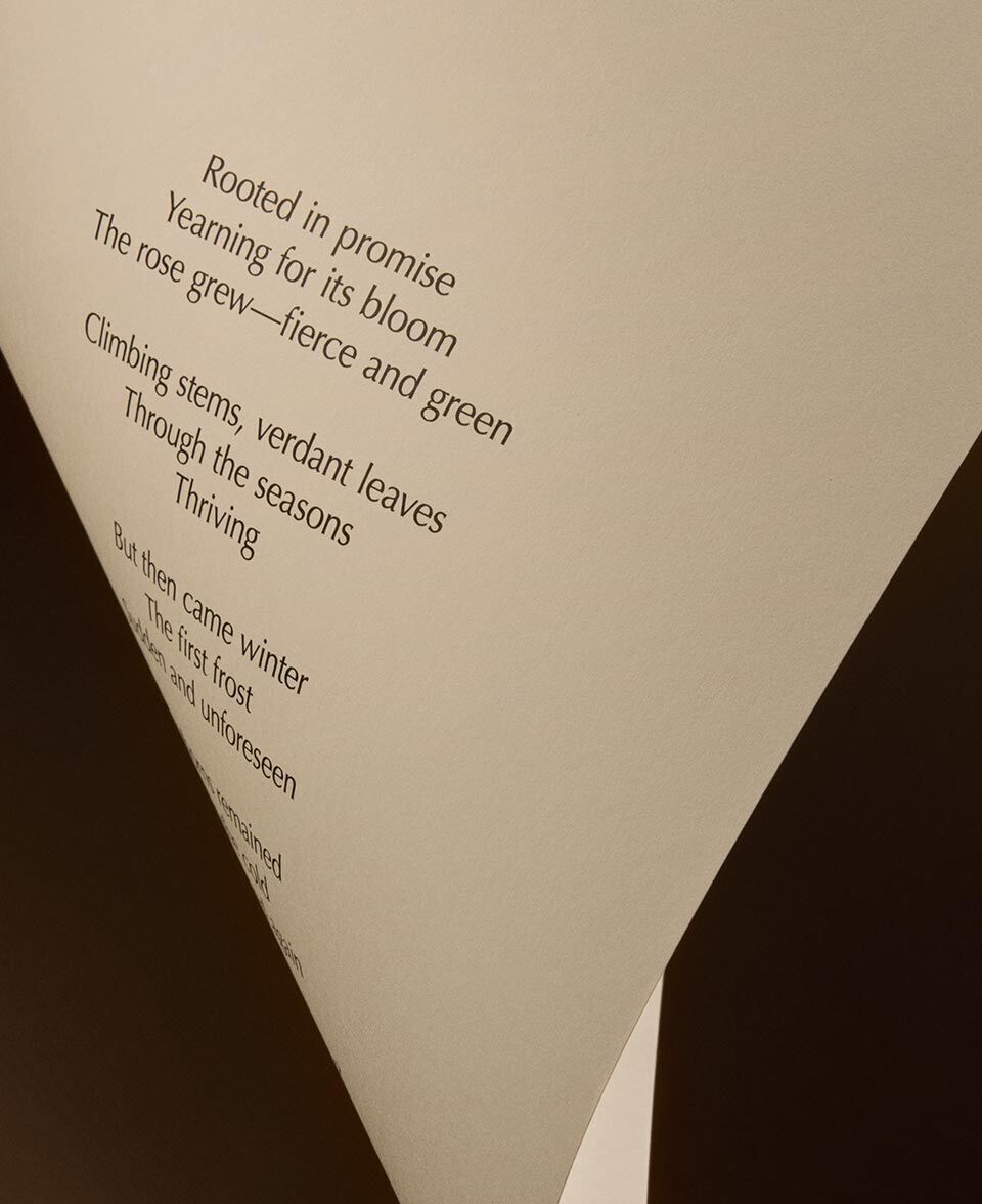 Pliegue triangular de papel crema que muestra el texto de un poema sobre un fondo oscuro.