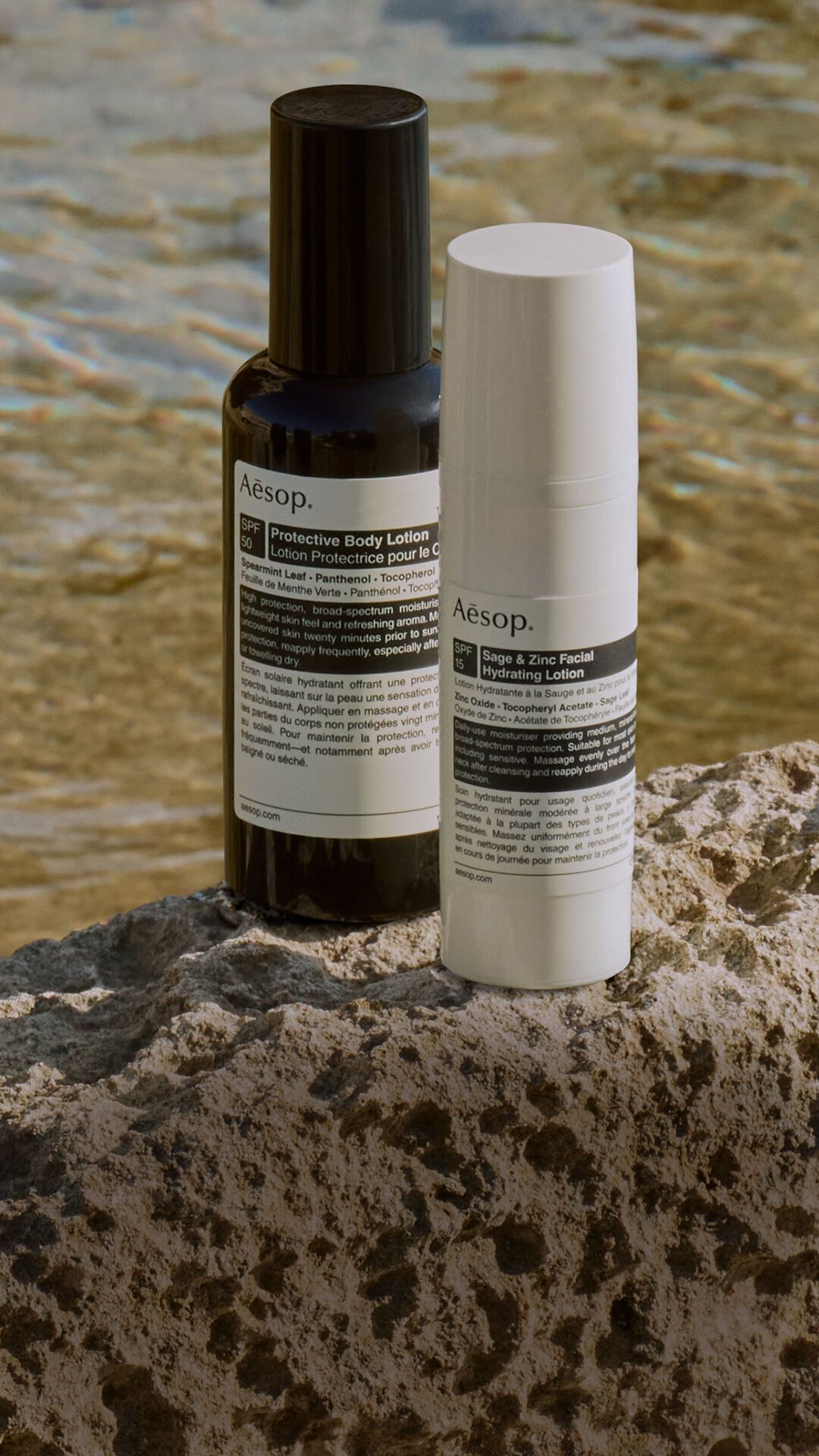 Una cuidada seleccion de formulaciones de proteccion solar de Aesop sobre una roca junto al mar.