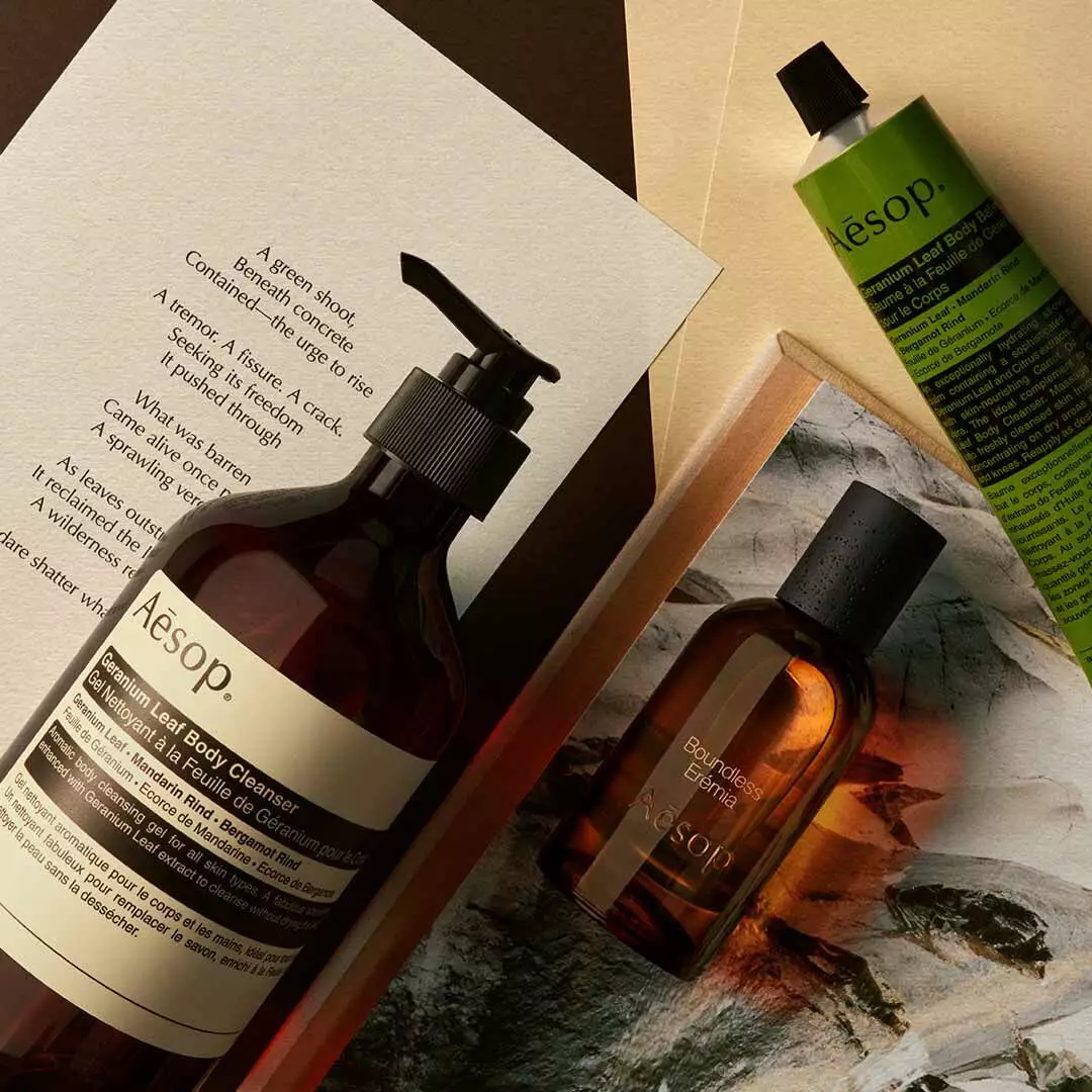 Frasco de Aesop Boundless Eremia con dispensador y tubo verde, dispuestos sobre papeles y una imagen de piedra.
